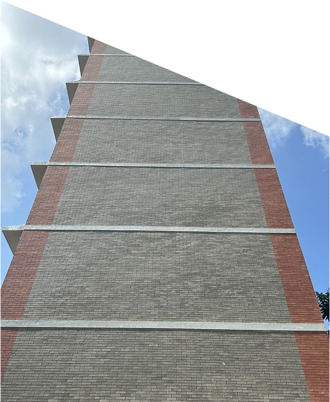 A tall brick building with red vertical stripes and horizontal white lines stretches upward. The top of the building is cut off by a sharp white angle, and the blue sky with clouds is visible on the left and right edges.